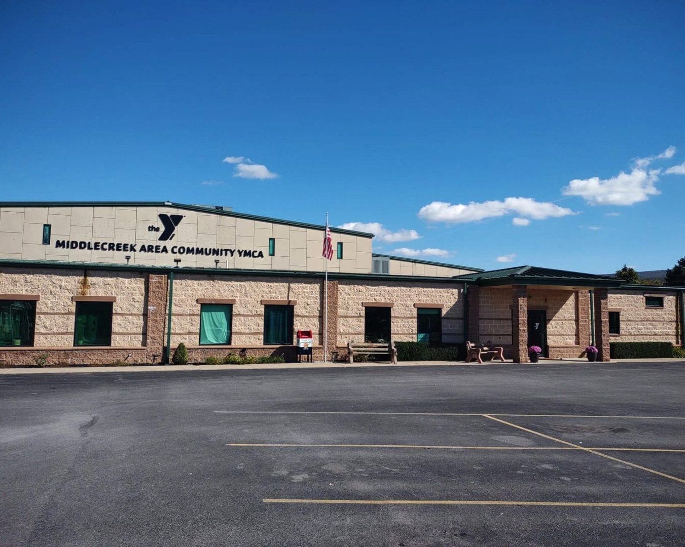 A photo of the Middle Creek Area Community Center. A tan building with a green roof and a parking lot out front.